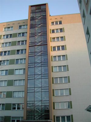 Hohe gläserne Liftschachtkonstruktion an der Fassade eines Mehrfamilienhauses