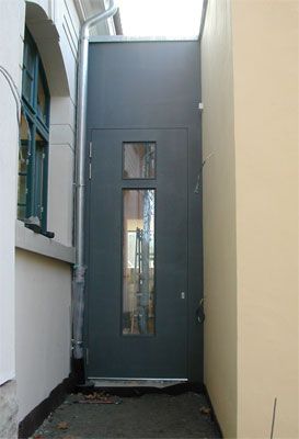 Graue Brandschutztür mit zwei Glasfenstern in einem engen Treppenhaus